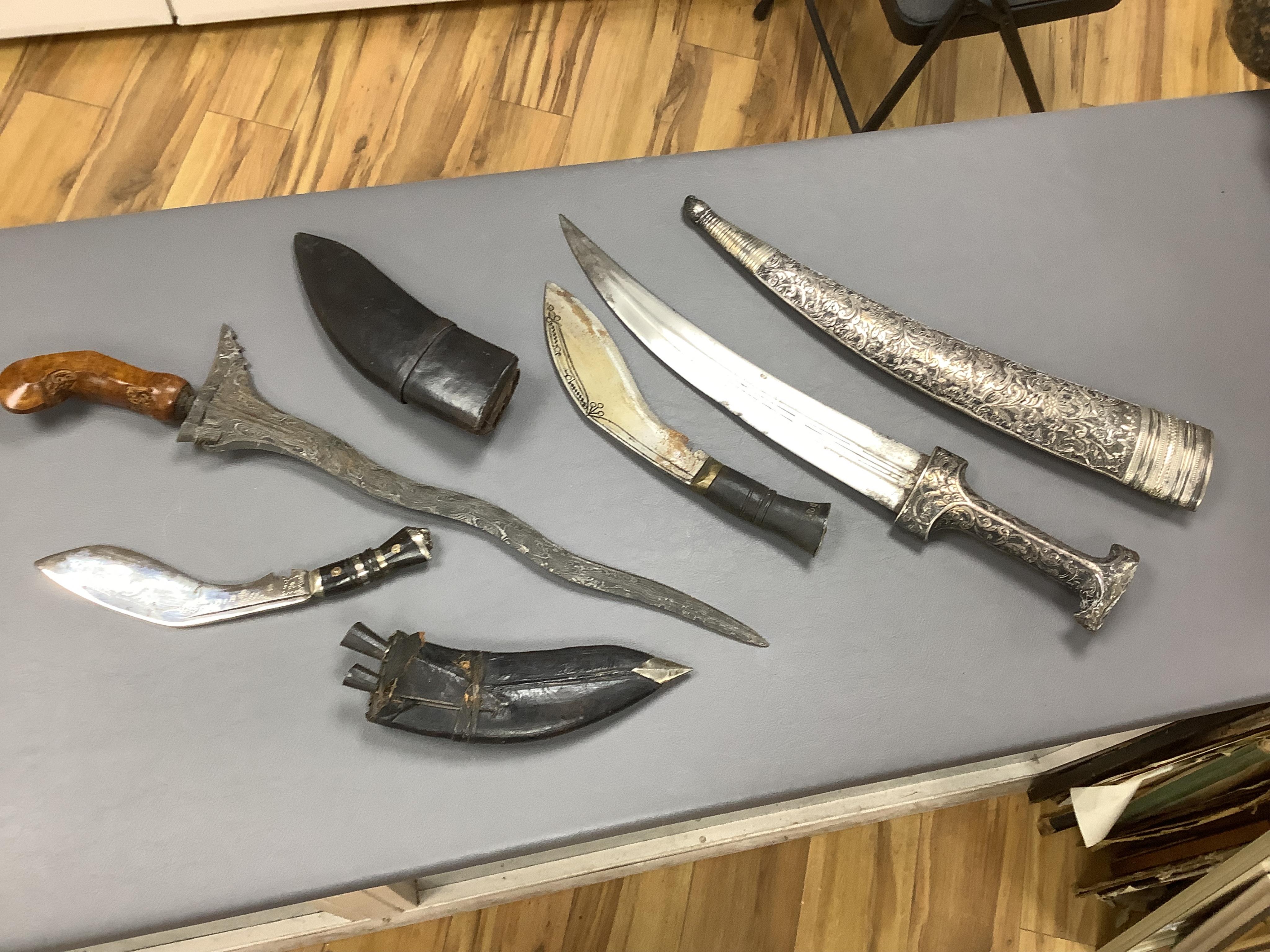 Eighteen assorted world weapons comprising a silver jambya (pommel missing), a knobkerry, a dha, two kris (one with handle missing), a lohar, three kukris, a djambok, a Chinese trousse, a chora, a flyssa, five others and